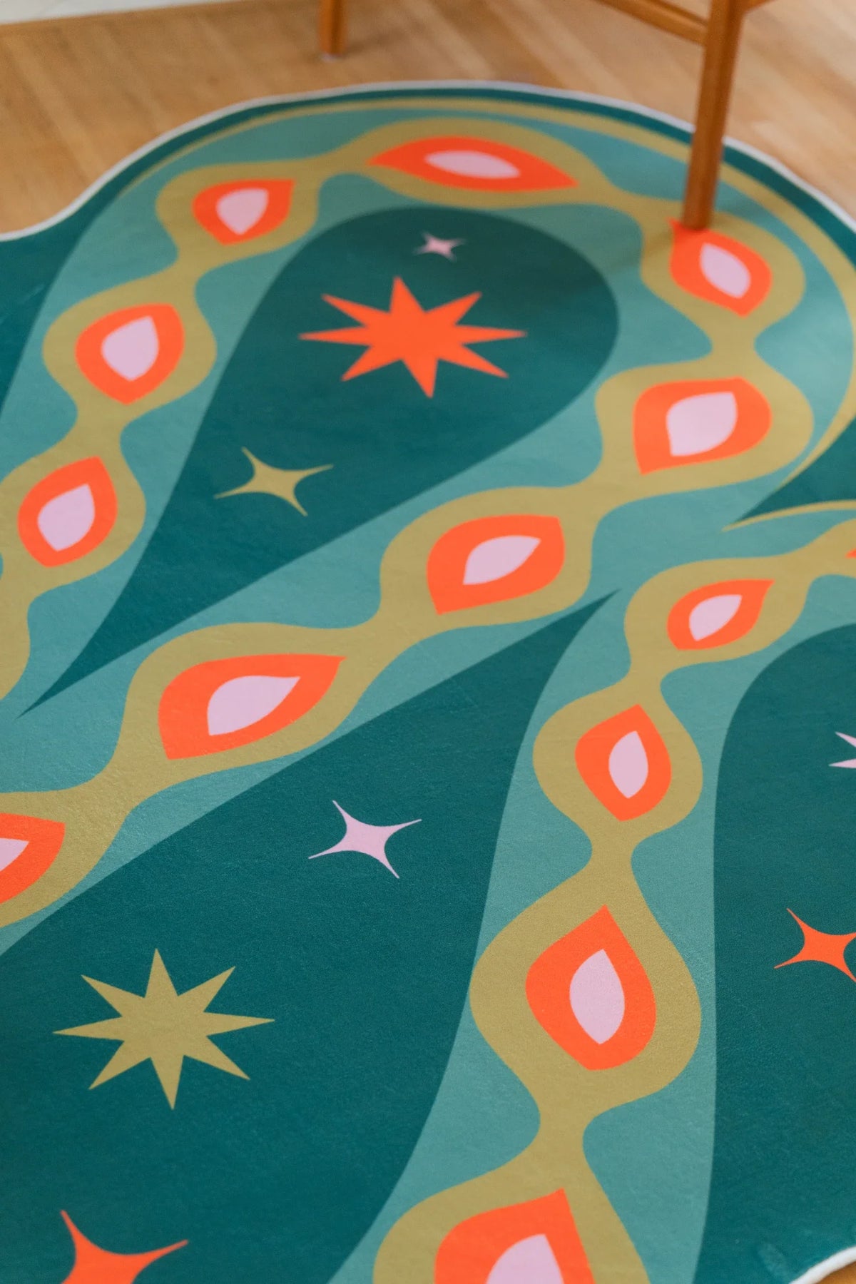 Detail of the deep green abstract rug with orange oval spots, pale stars, and a winding snake silhouette
