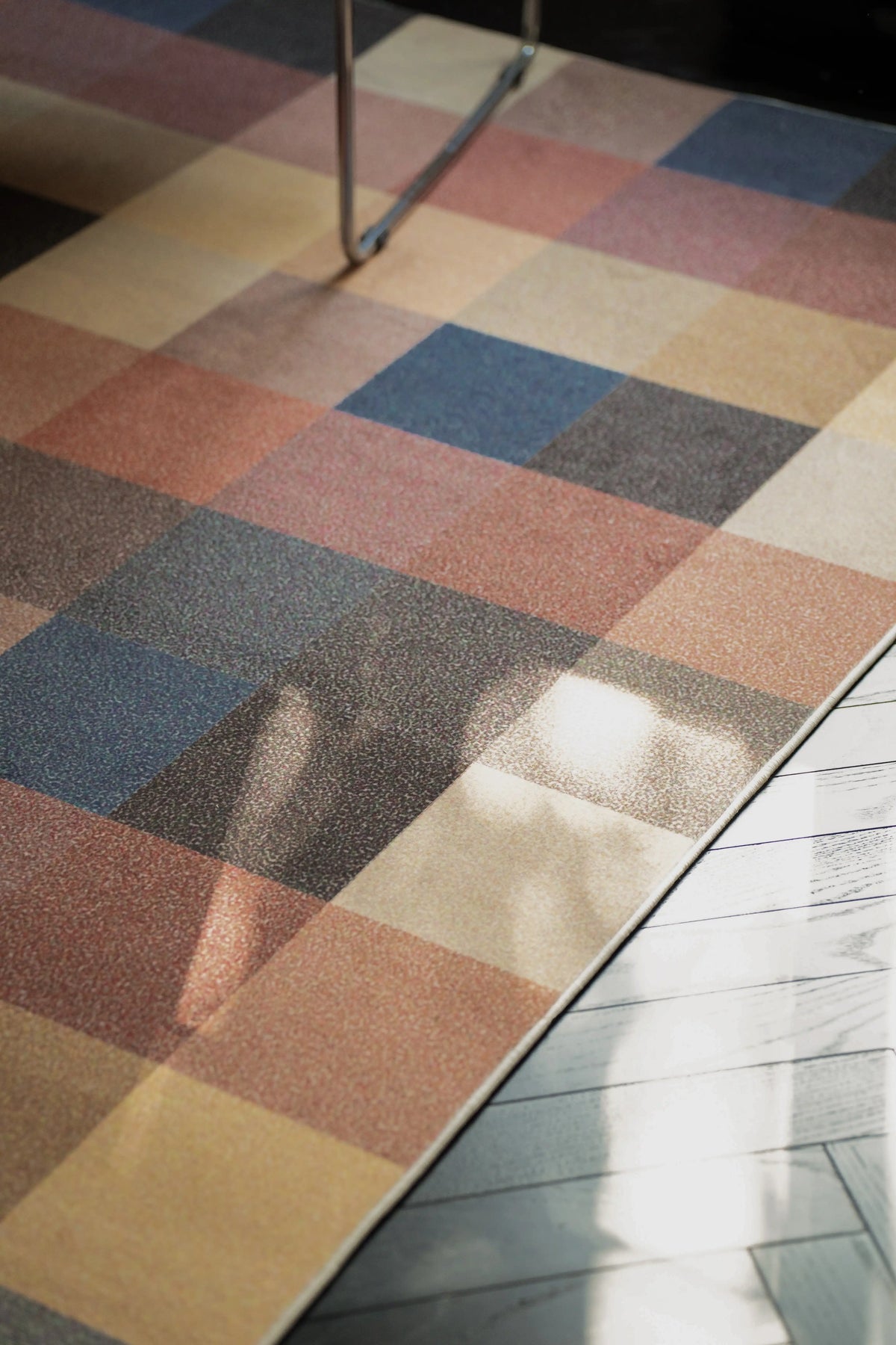 Close up of the vintage checkered rug with sunlight across the pattern and a chair leg at the edge