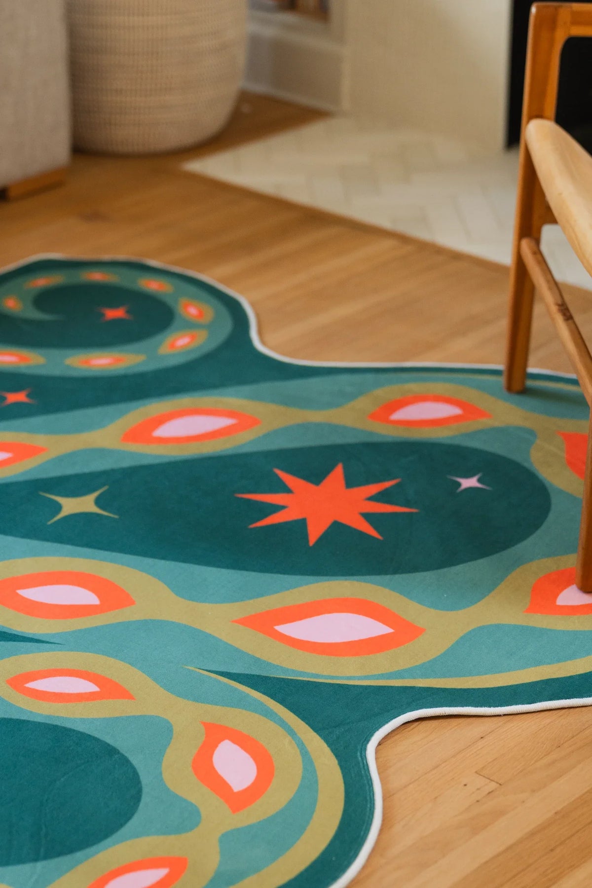 Close up of the dark green irregular rug on a light wood floor, showing the snake body with orange and cream accents