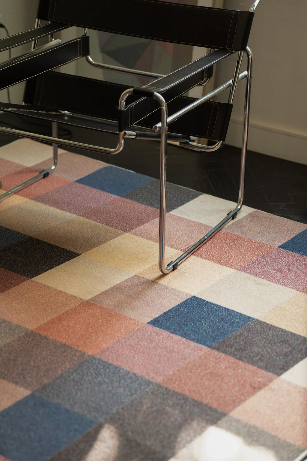 Juan Marquez checkered rug under a chrome chair with earthy brown, rust, blue, and cream grid blocks