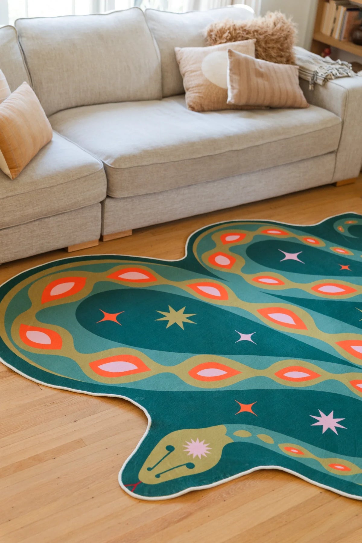 Green snake shaped area rug under the sofa edge, showing the head, white eye, and curved striped body