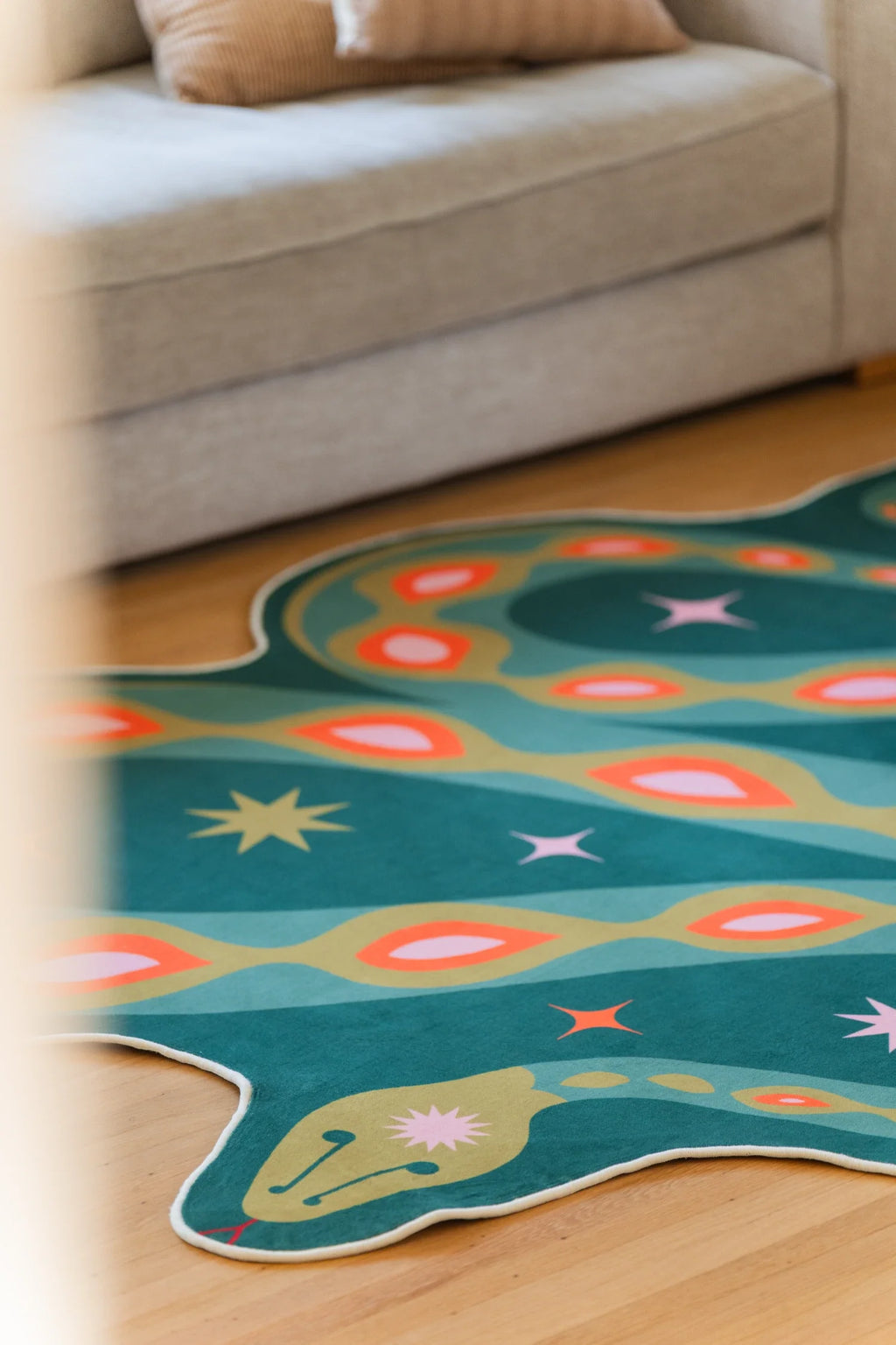 Close crop of the green rug beside a beige sofa, highlighting small star motifs and flowing snake contours