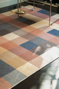 Vintage checkered rug beneath a chrome chair with sunlight falling across the earthy color block pattern