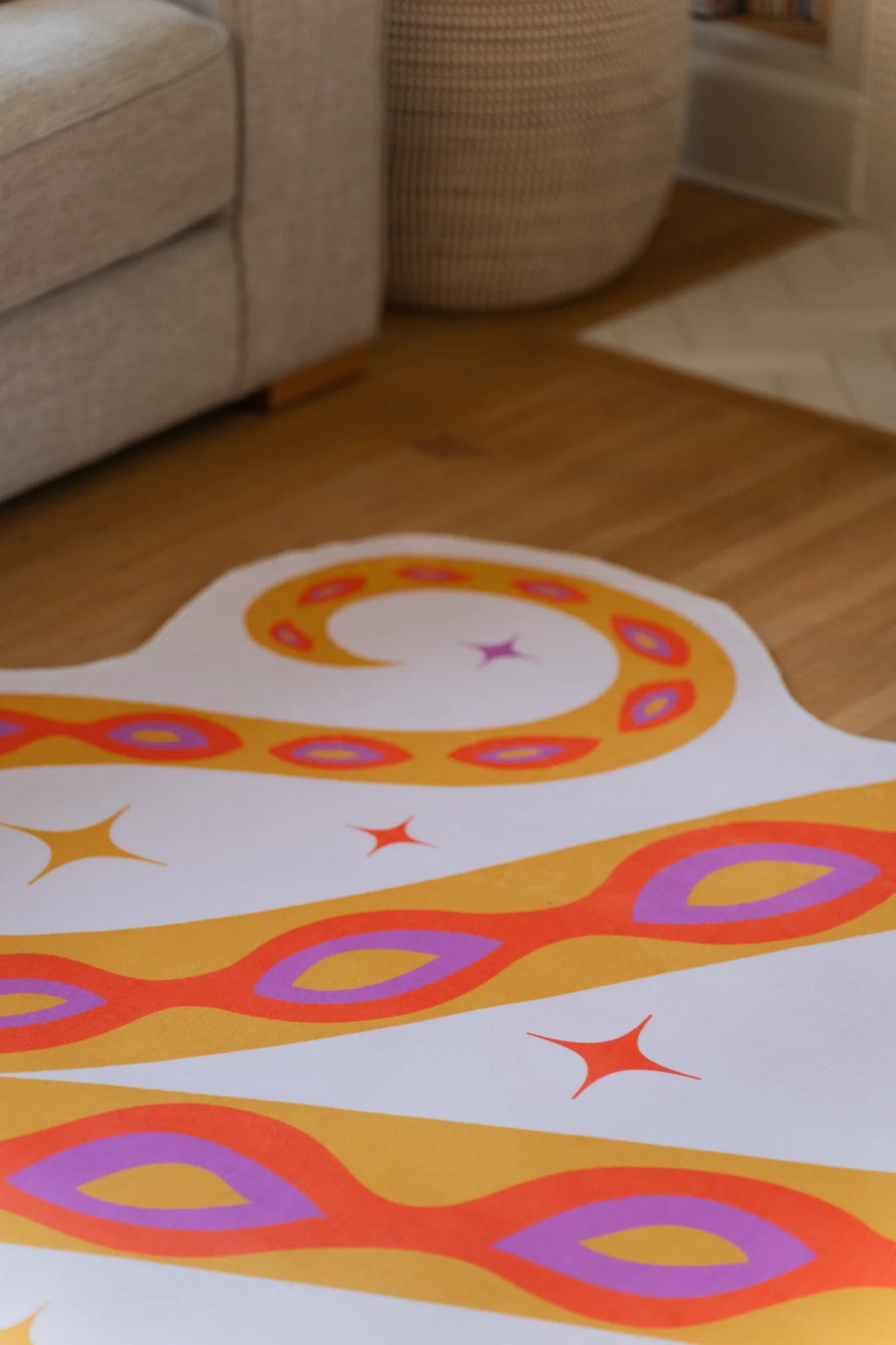 Close up of the orange abstract rug beneath a beige sofa, showing curved snake coils, a star motif, and oval spots
