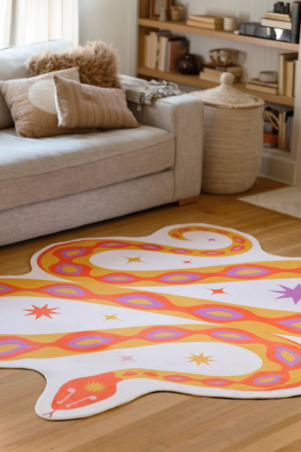 Orange abstract snake rug beside a beige sofa, showing rounded coils and eye like markings on a pale ground