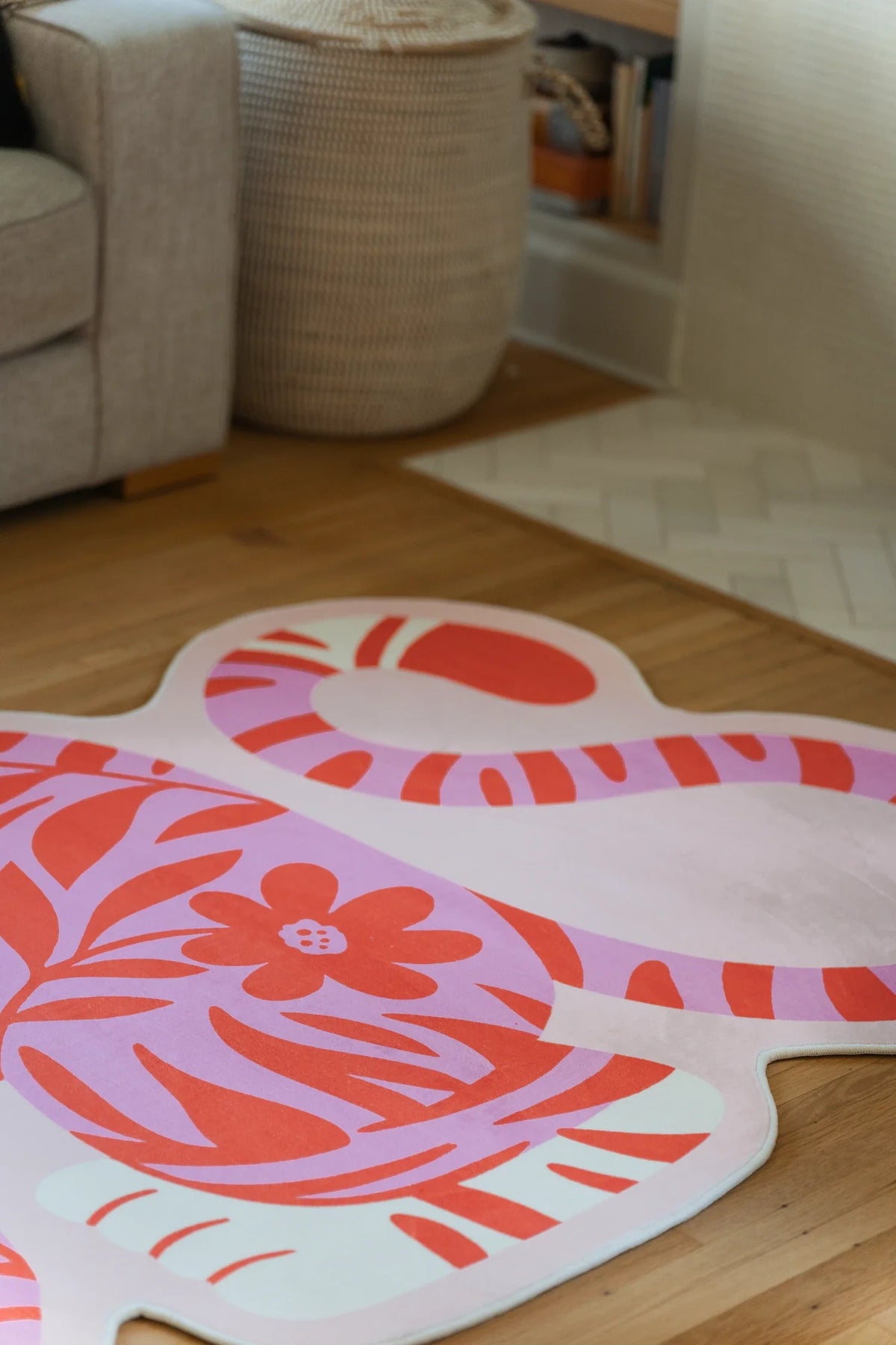 Pink vintage tiger rug beside a woven basket and wood chair, with floral linework across the crouched body
