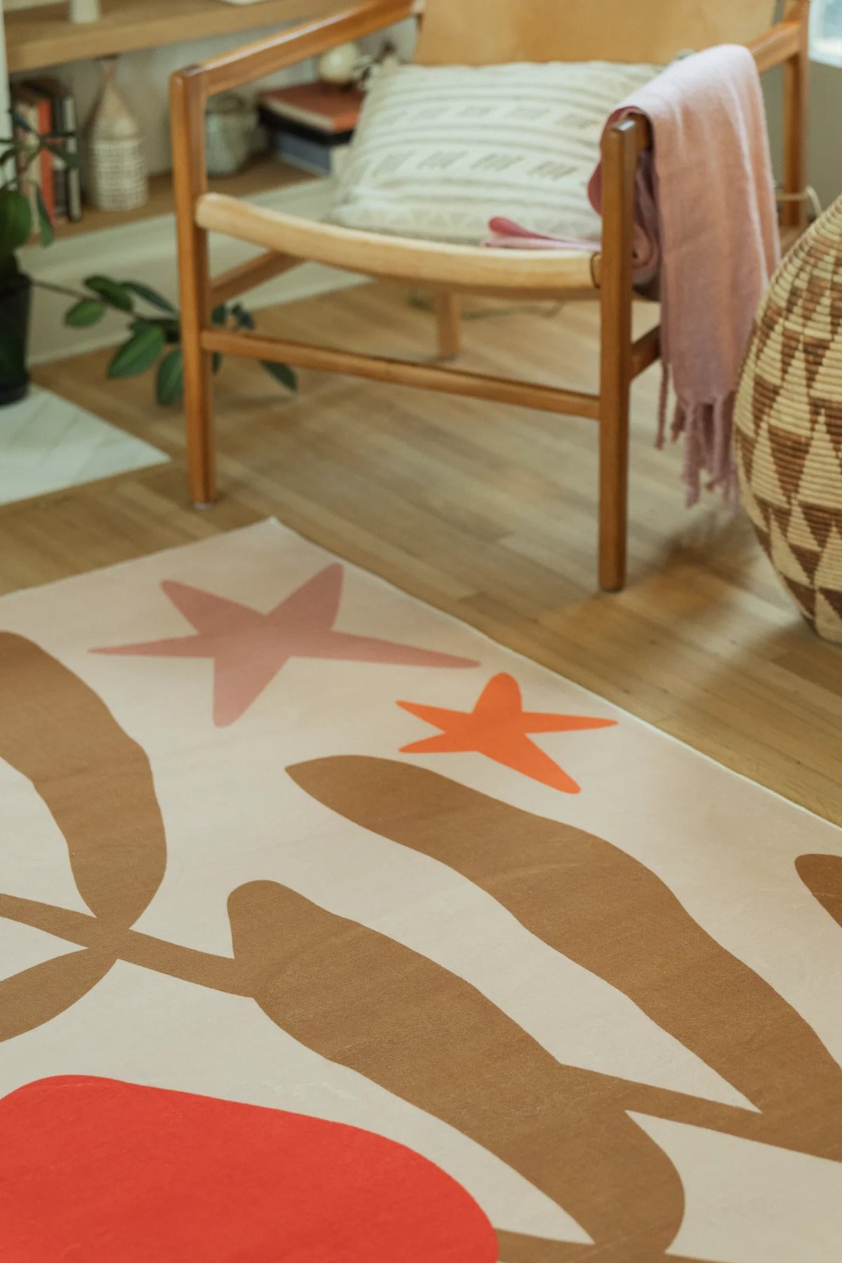 Close view near the chair with soft geometric blocks, tan stems, and red petal shapes on the cream field
