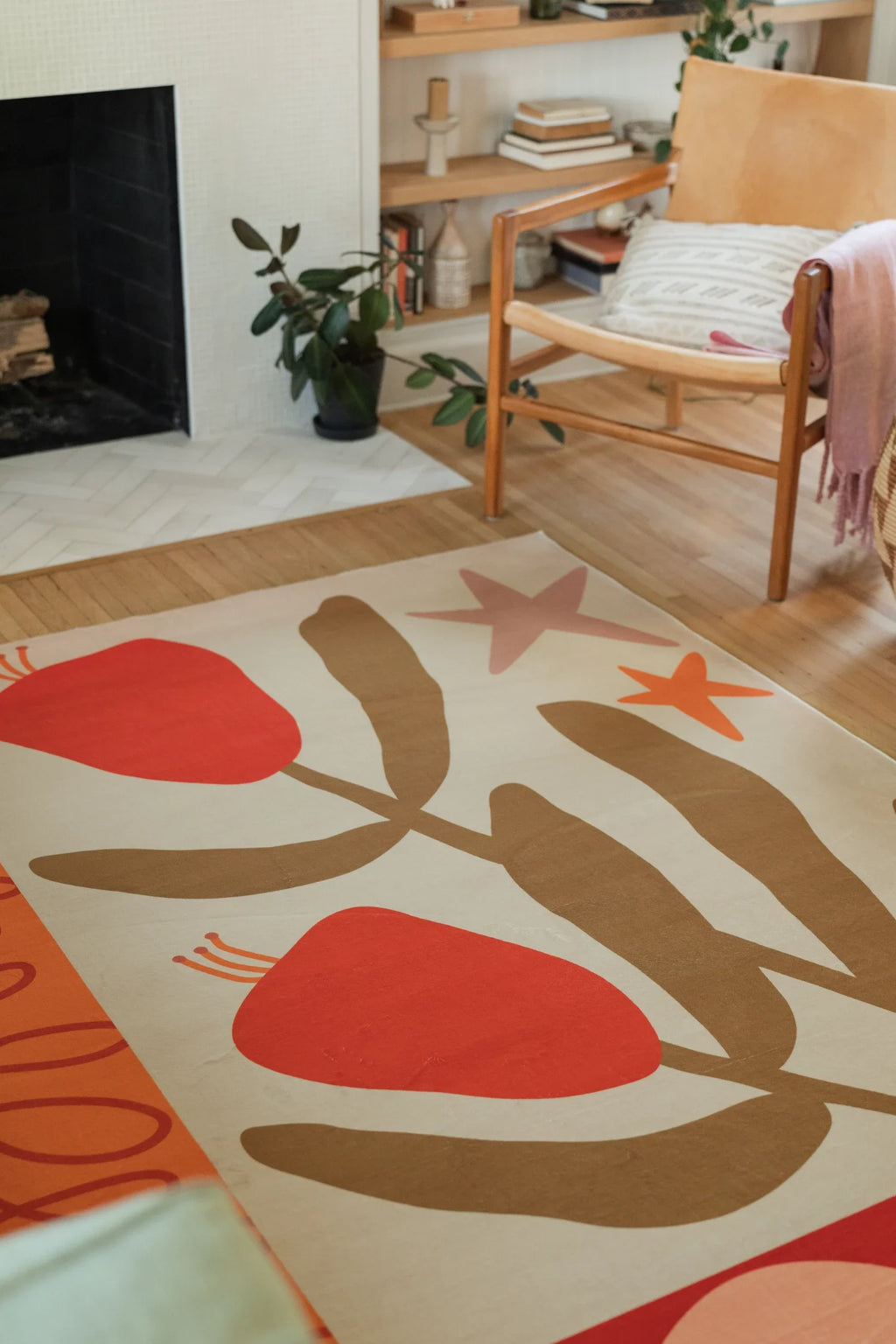 Partial rug view in front of the fireplace, with red floral forms, tan branches, and a small orange star