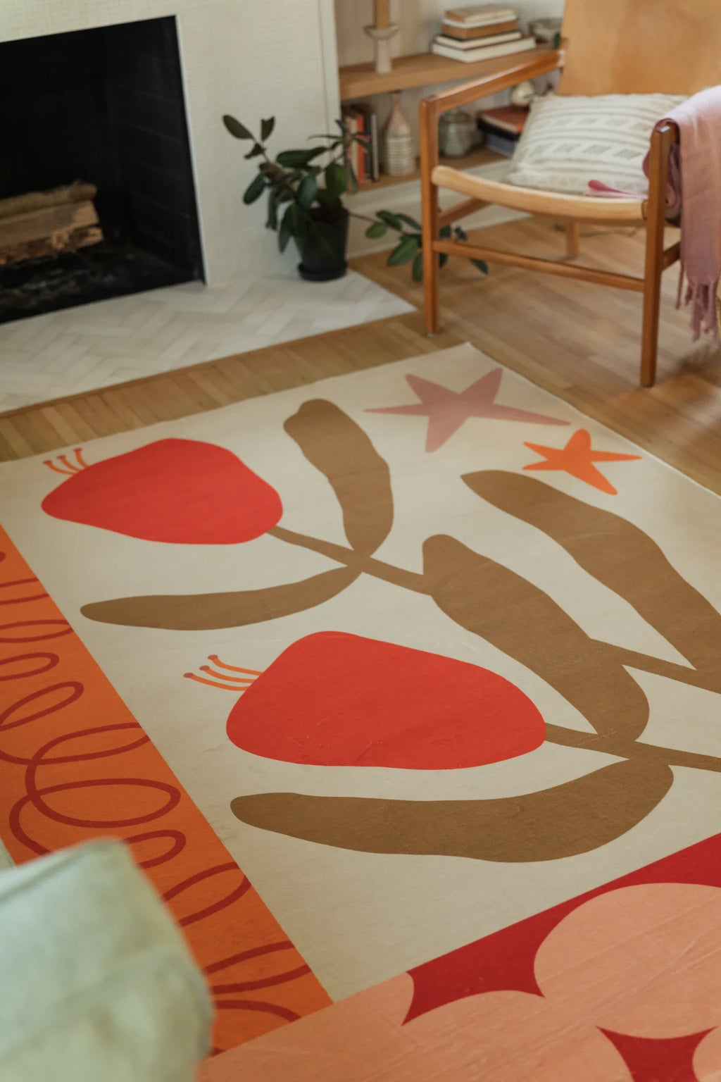 Vertical room crop of the rug beside a wood chair and fireplace, showing the central flower and stem composition