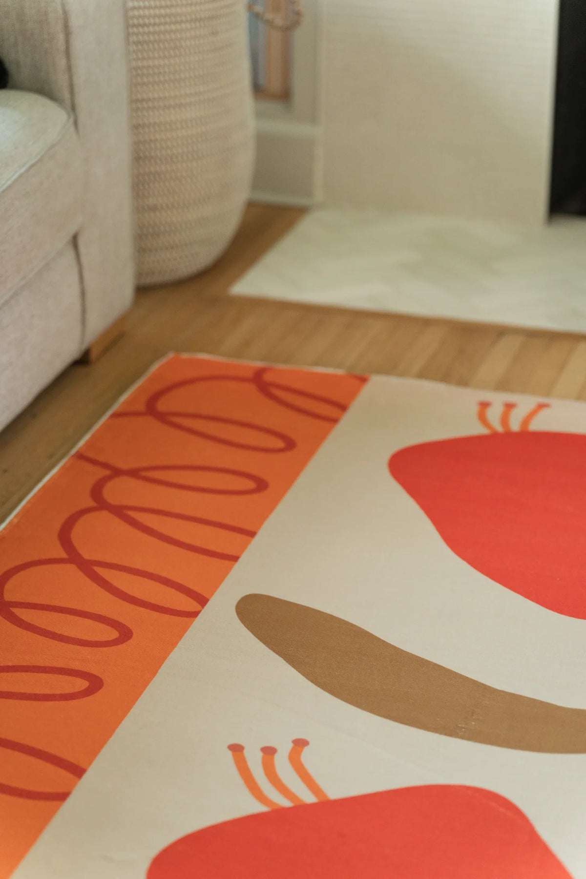 Vertical crop under the sofa showing the orange line border, tan stem, and red flower head on a cream ground