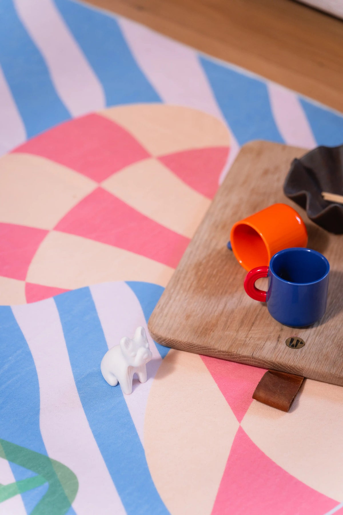 Orange and blue cups on a wooden board over blue-and-white stripes and a pink check pattern on the rug.