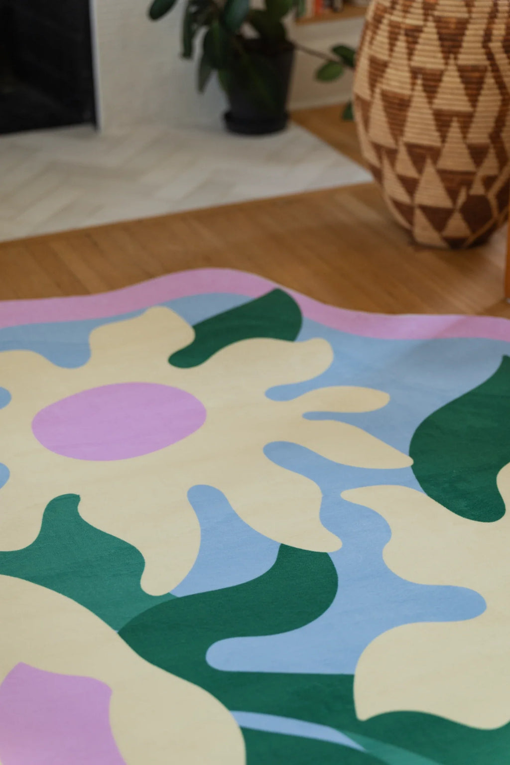 Colorful floral rug on a light wood floor beside a woven basket, with lilac petals and cream shapes on a pale blue ground