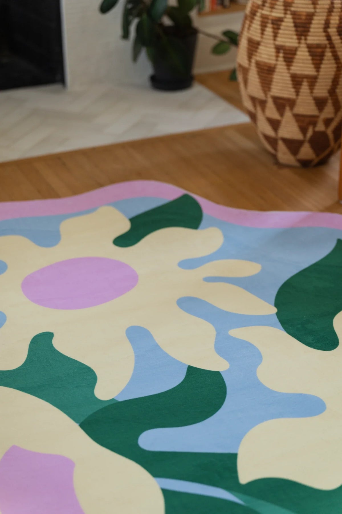 Colorful floral rug on a light wood floor beside a woven basket, with lilac petals and cream shapes on a pale blue ground