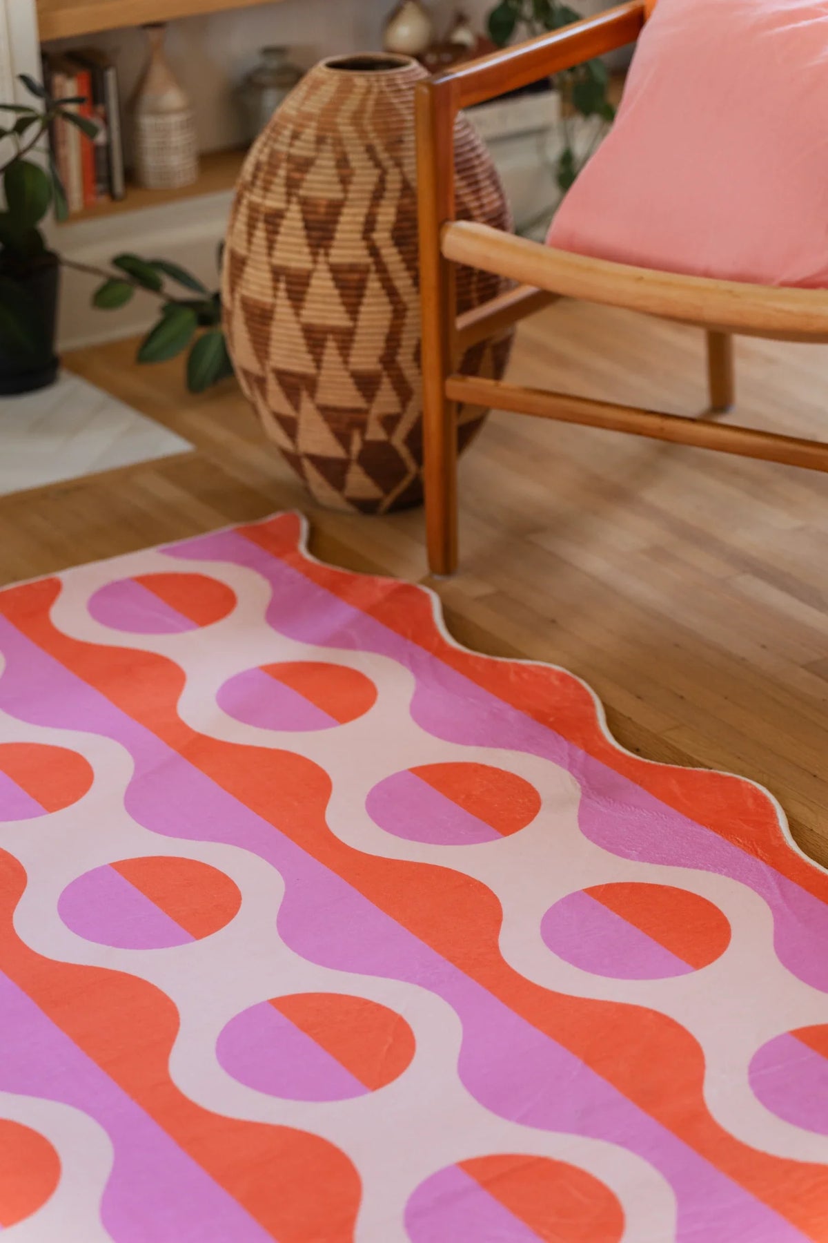 Close crop of the pink geometric rug beside an orange chair and woven basket on a light wood floor