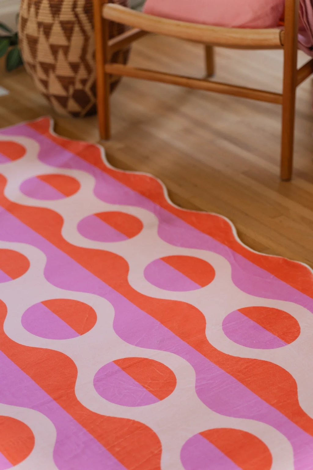 Partial view under a wood chair, with coral and pink stripes meeting the rug's softly scalloped edge