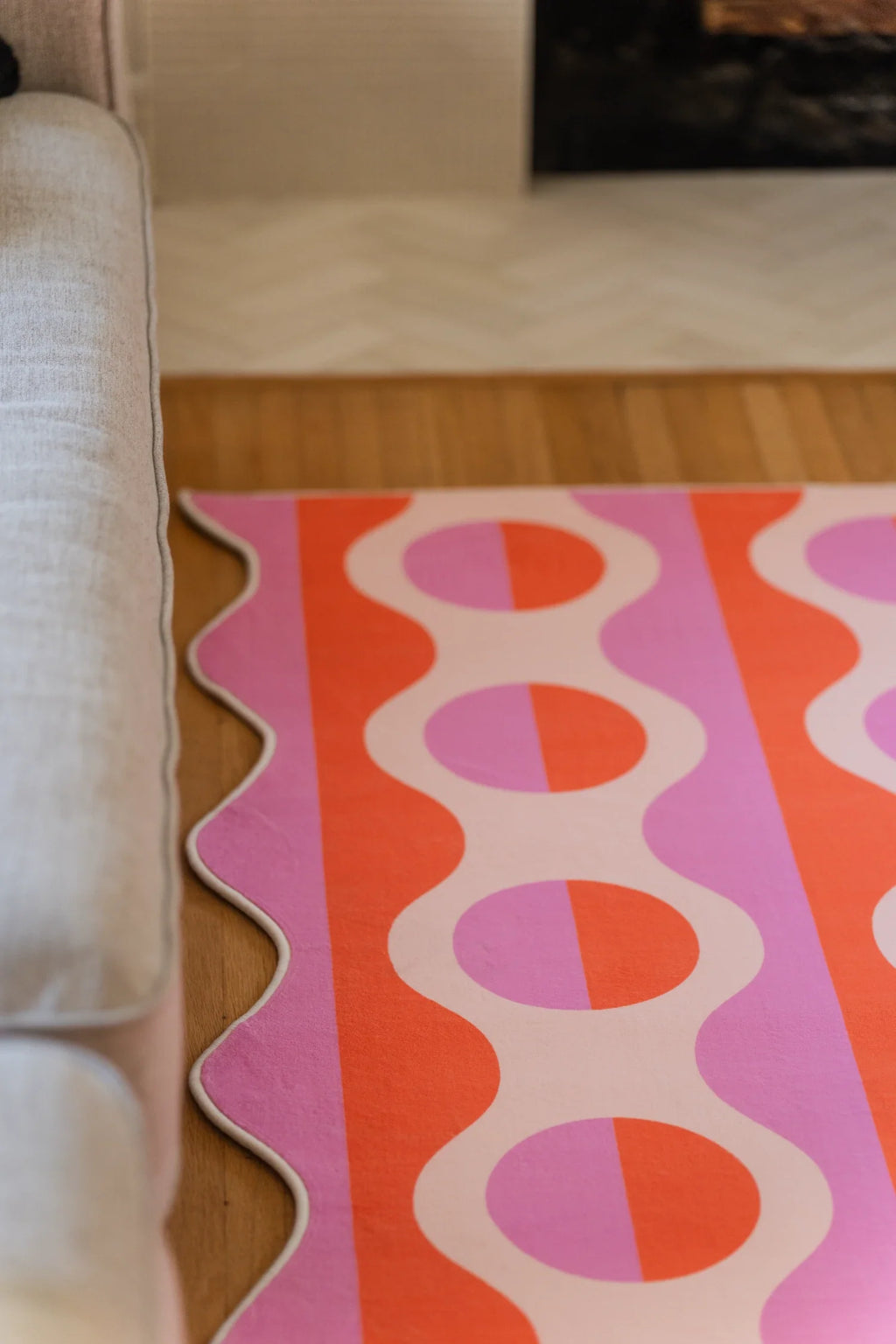 Pink geometric striped rug beneath the sofa edge, with orange oval shapes aligned in vertical rows