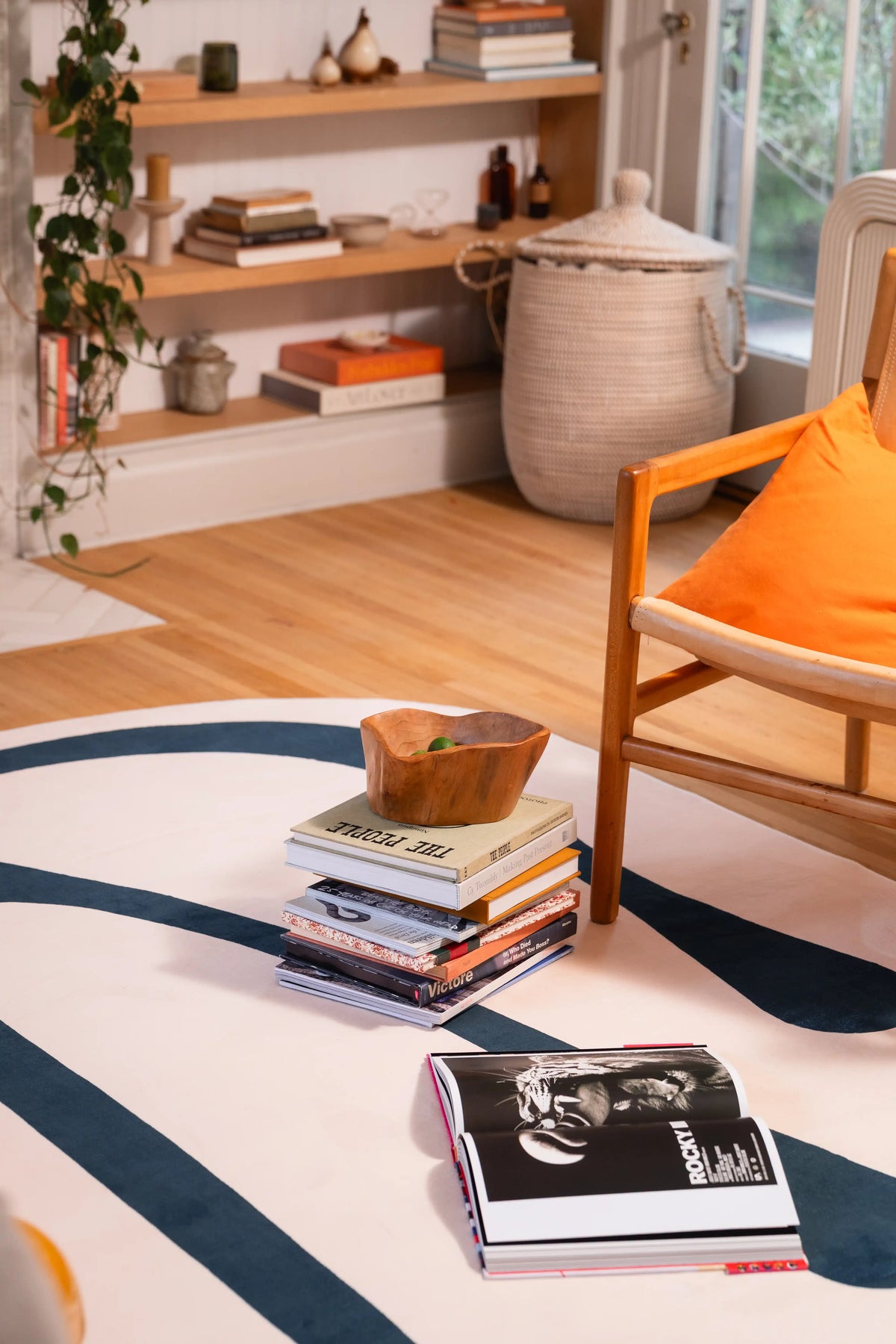 Close-up of a deep green drip-pattern rug with stacked books, a wooden bowl, and black art book.