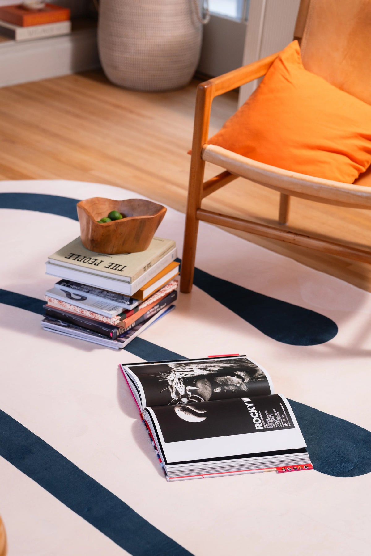 Deep green curve across a beige rug beneath a wooden armchair with stacked books and a wooden bowl.