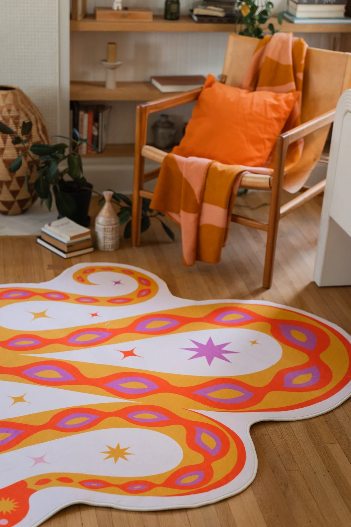 Orange abstract snake rug beside a wood chair with an orange pillow, adding a bold focal point to the floor