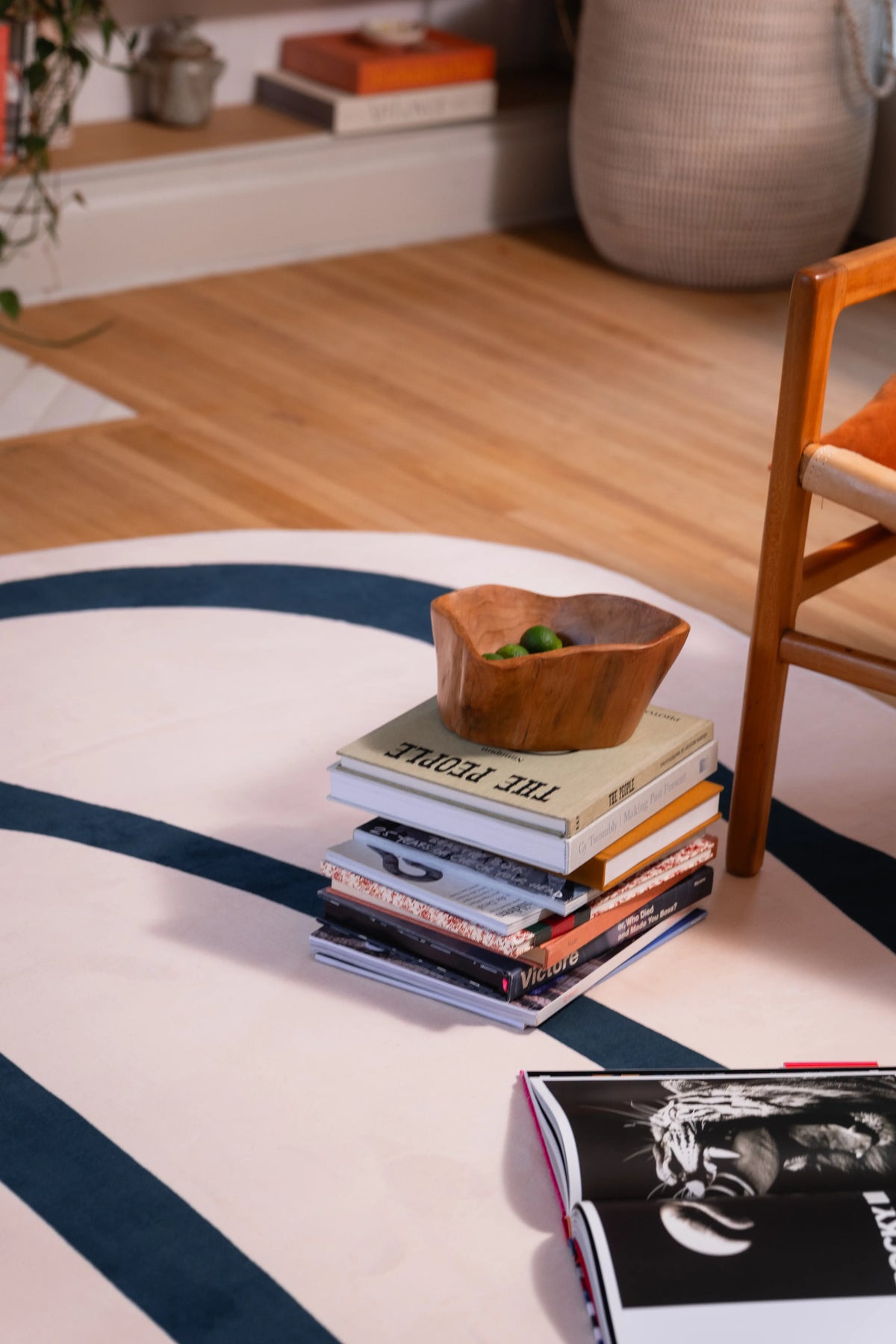 Close-up of stacked books and a wooden bowl resting on a beige rug with deep green lines.