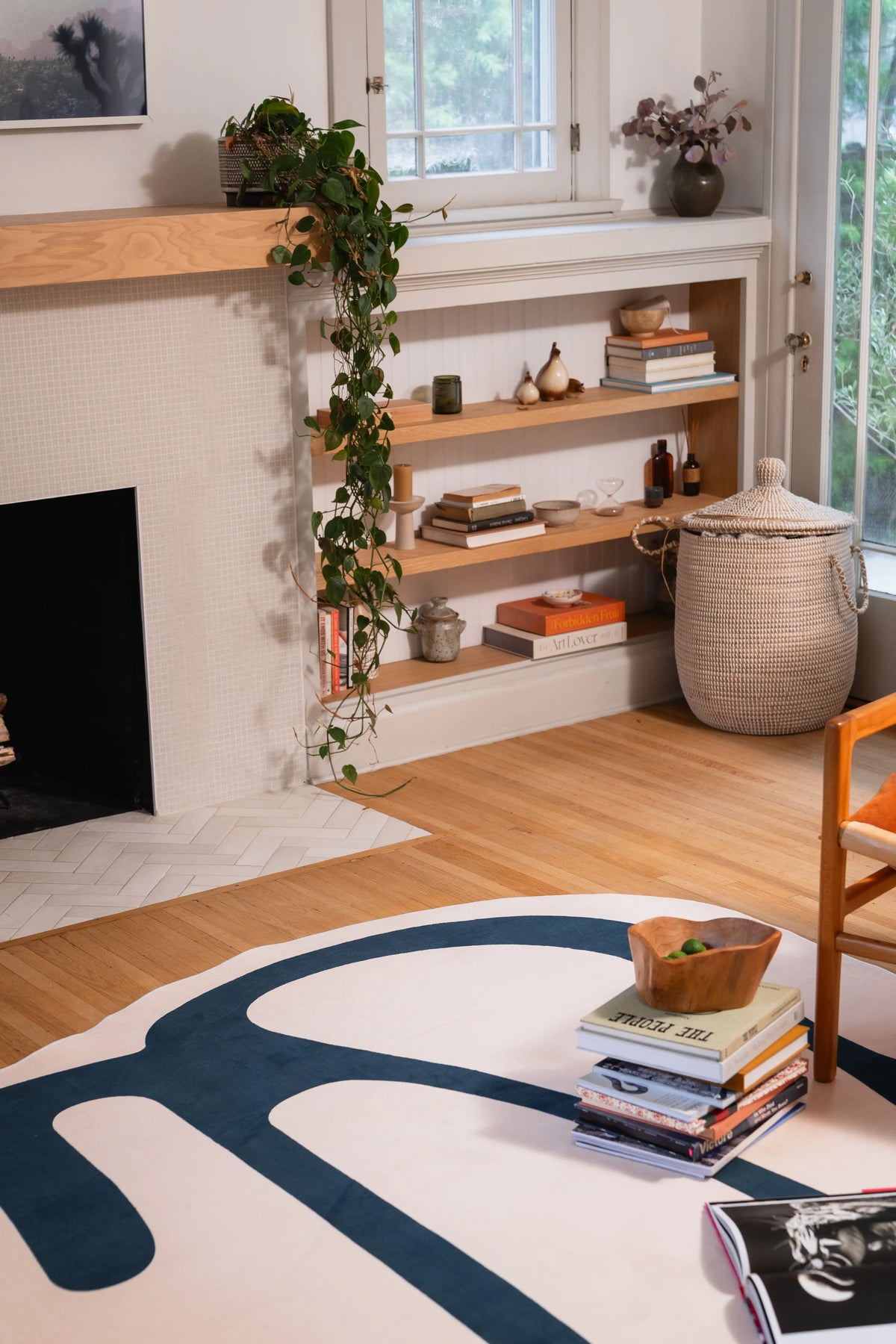 Beige graphic rug beside a fireplace and wooden chair, with stacked books resting on its deep green curves.