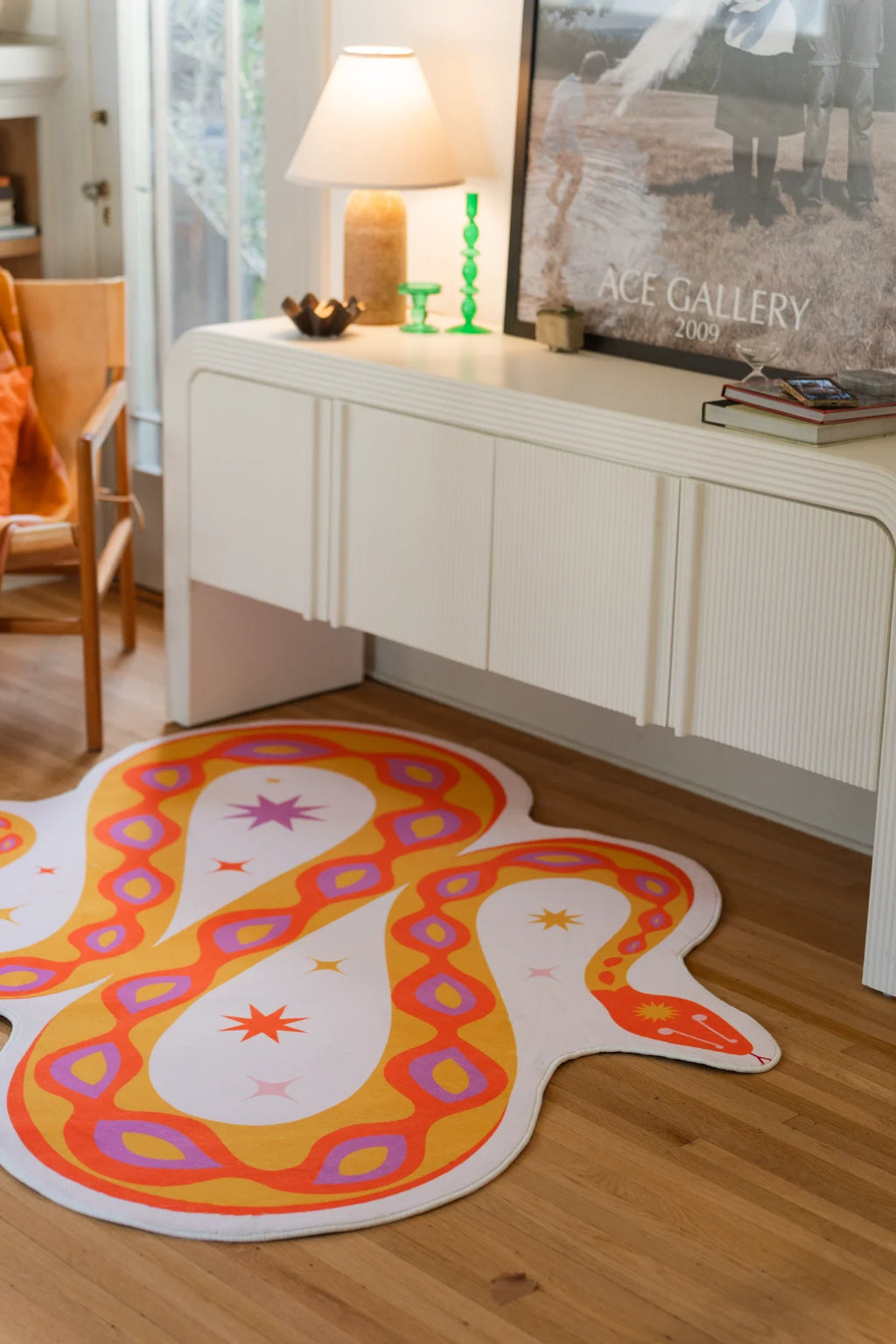 Snake shaped area rug next to a white media console and framed art, with an orange body and pink outlined markings