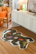 Green animal shaped crocodile rug on a light wood floor beside a white media console and orange chair