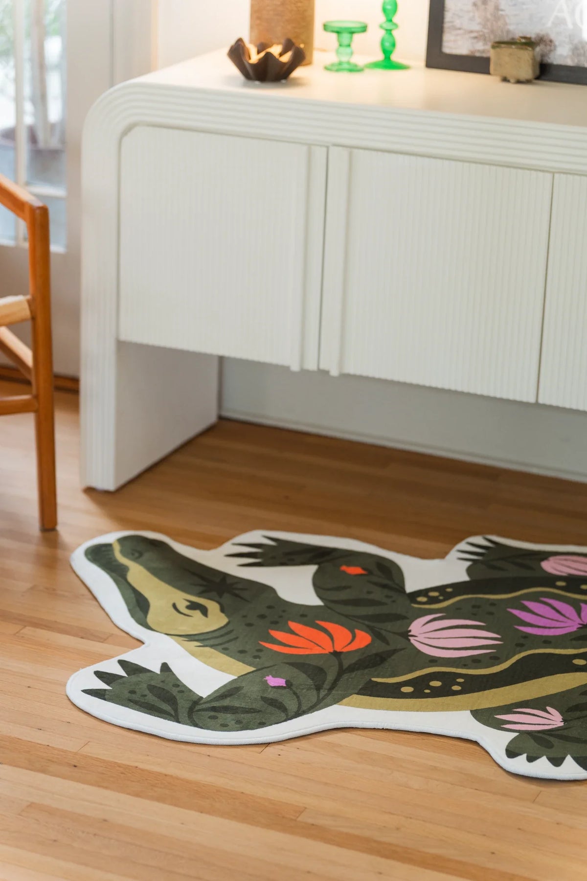 Partial view of the green crocodile rug on a light wood floor, with a long tail and floral motifs across the back