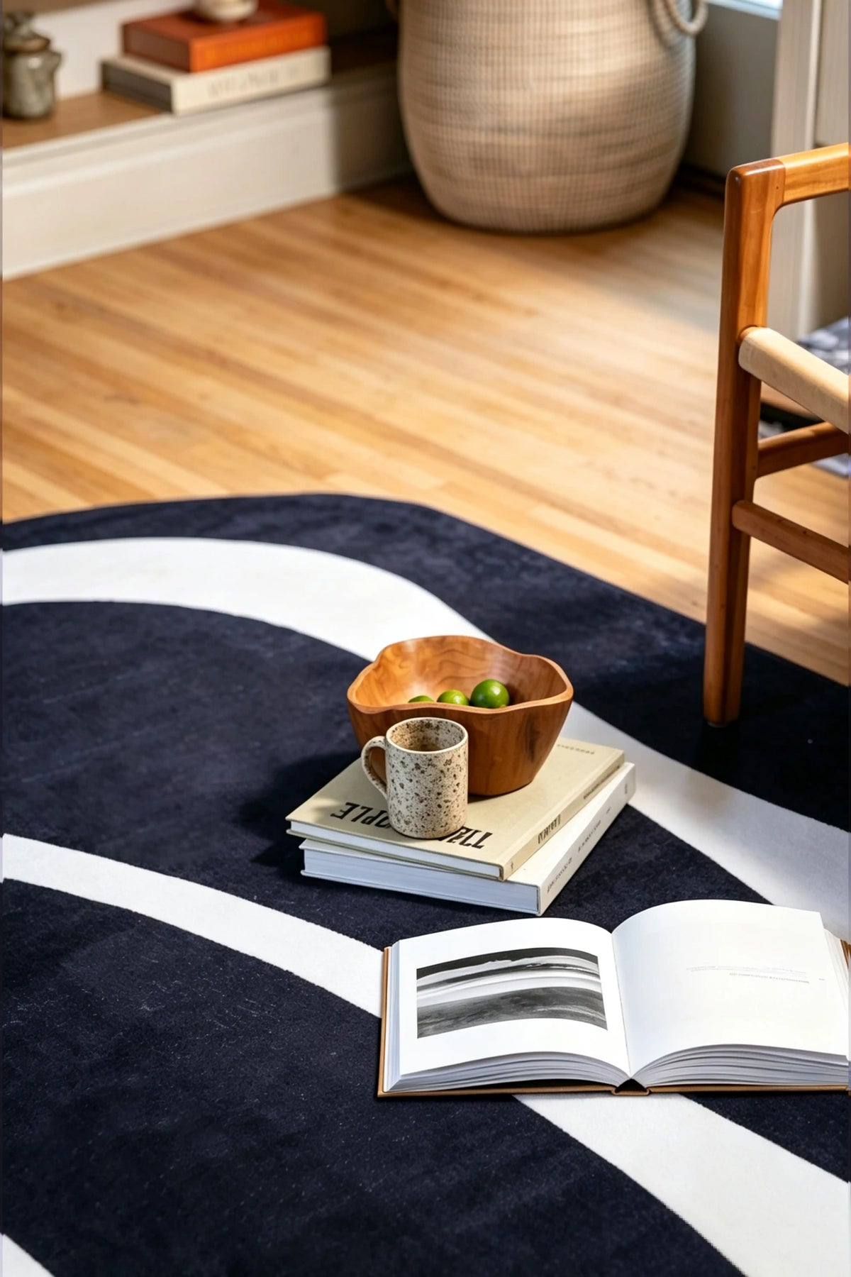 Close-up of a black graphic rug beneath a wooden chair with an open book and small wooden bowl.