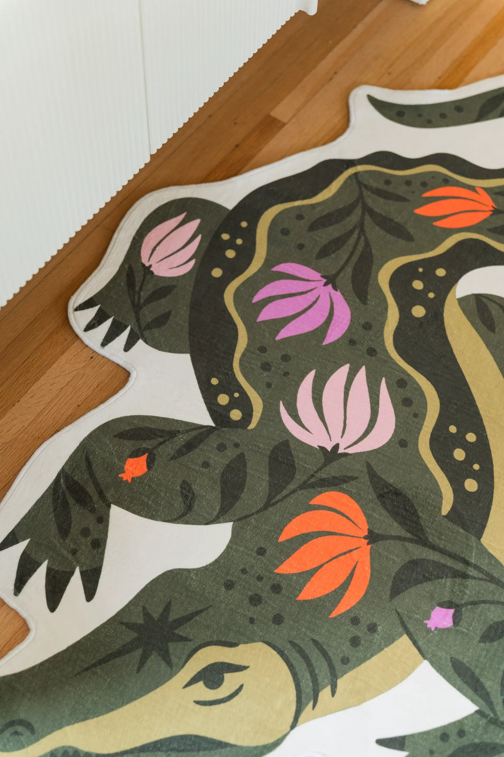 Close up of the crocodile shaped rug showing the green snout, striped body, and pink floral detailing