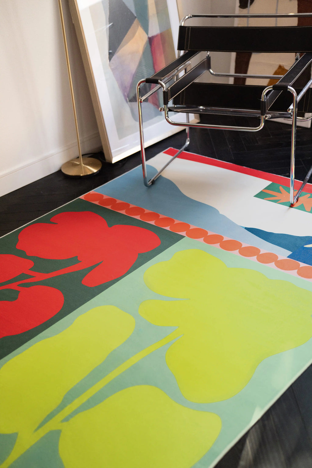 Close up of the flower rug under a chrome chair, showing red blooms, lime green shapes, and a pale blue field