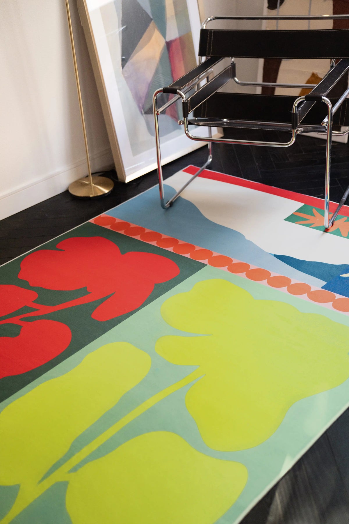Close up of the flower rug under a chrome chair, showing red blooms, lime green shapes, and a pale blue field