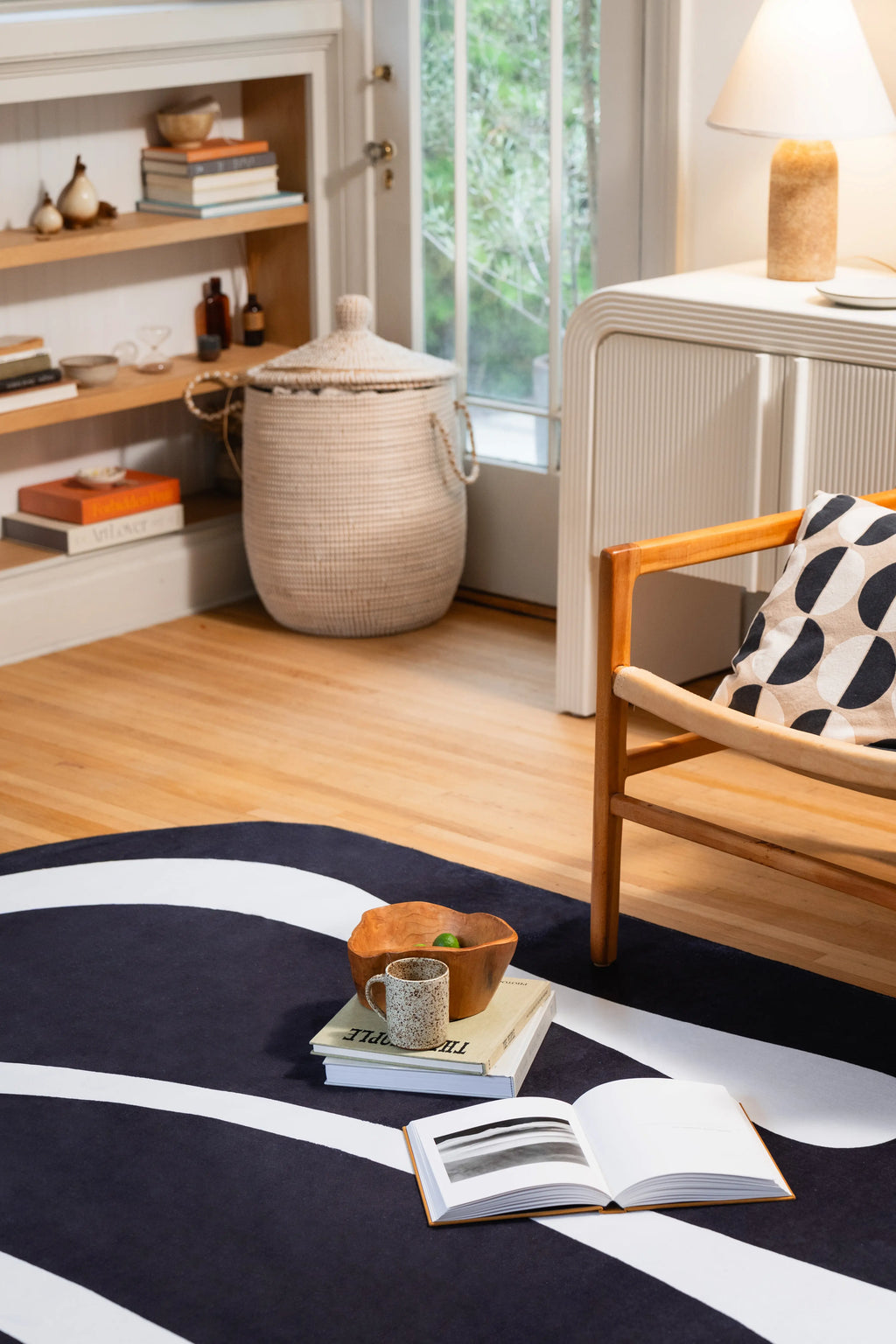 Black area rug with a sweeping white curve beside a wooden armchair, open book, and stacked books.