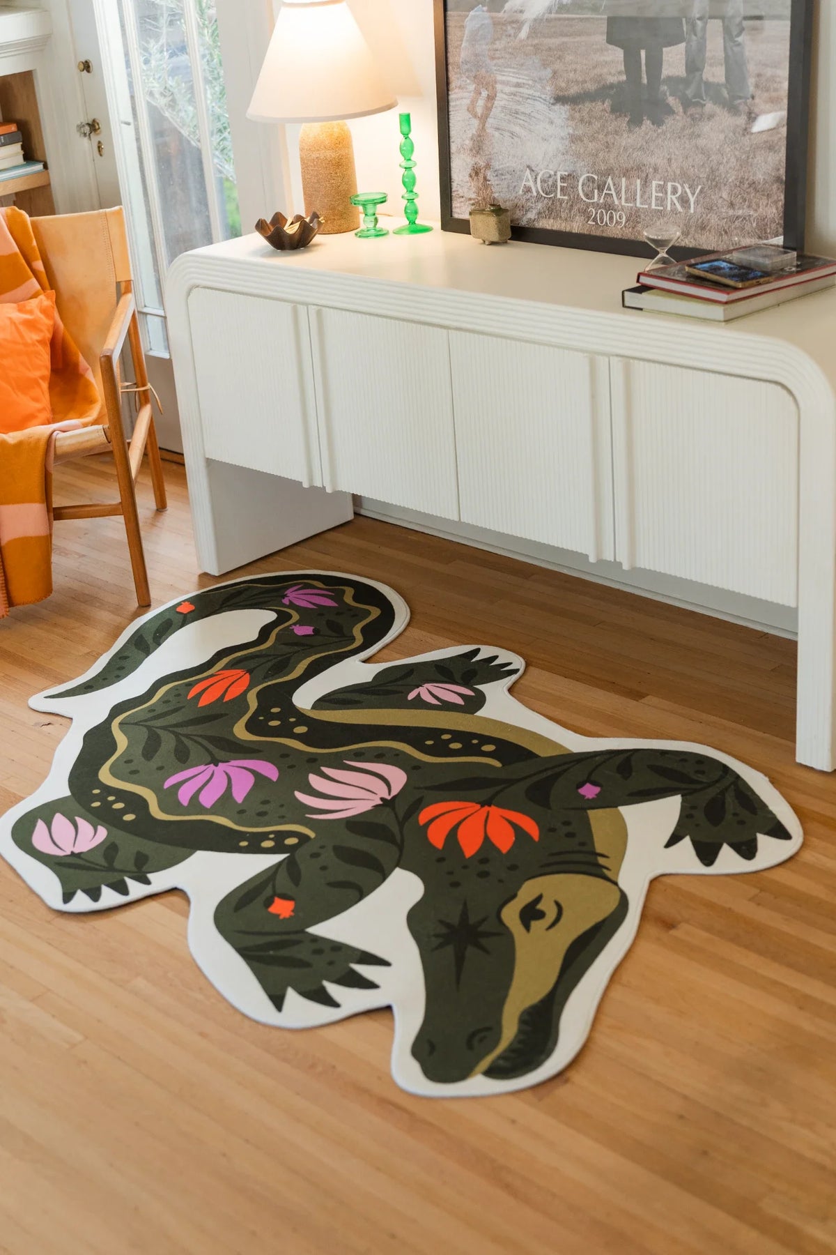 Green crocodile rug stretched in front of a white media console, showing pink flowers and orange botanical accents