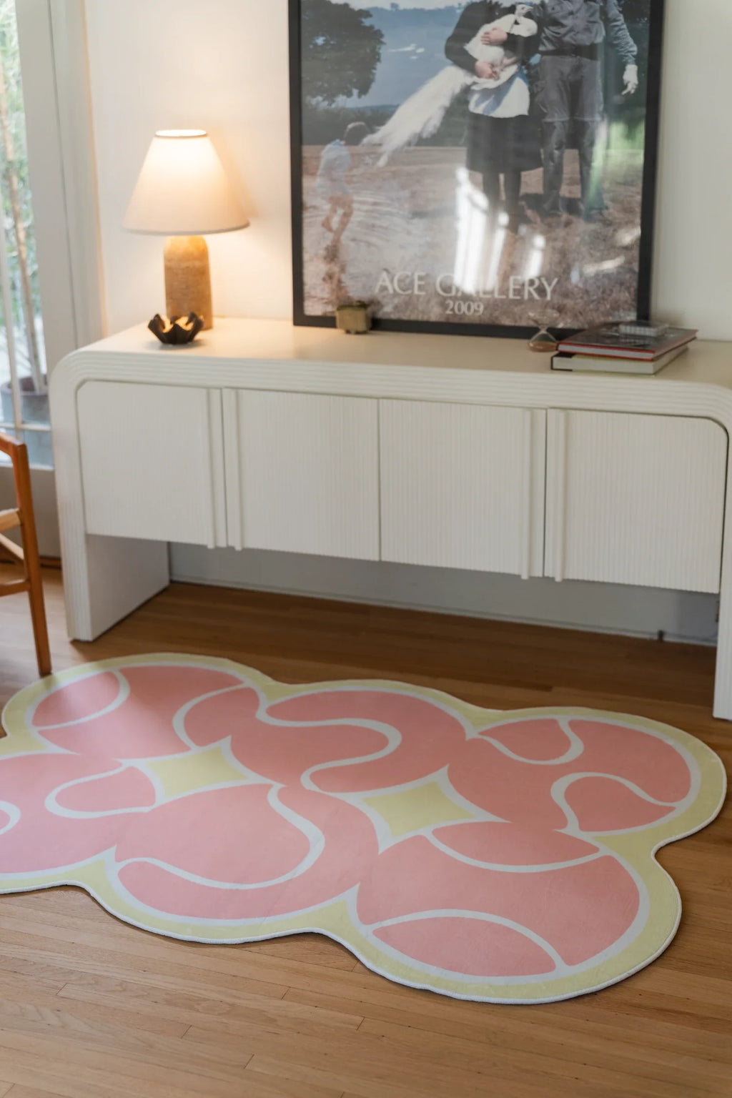 Pink irregular rug in front of a white media console with a lamp and framed artwork