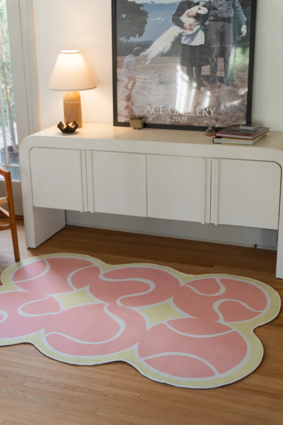 Pink irregular rug in front of a white media console with a lamp and framed artwork