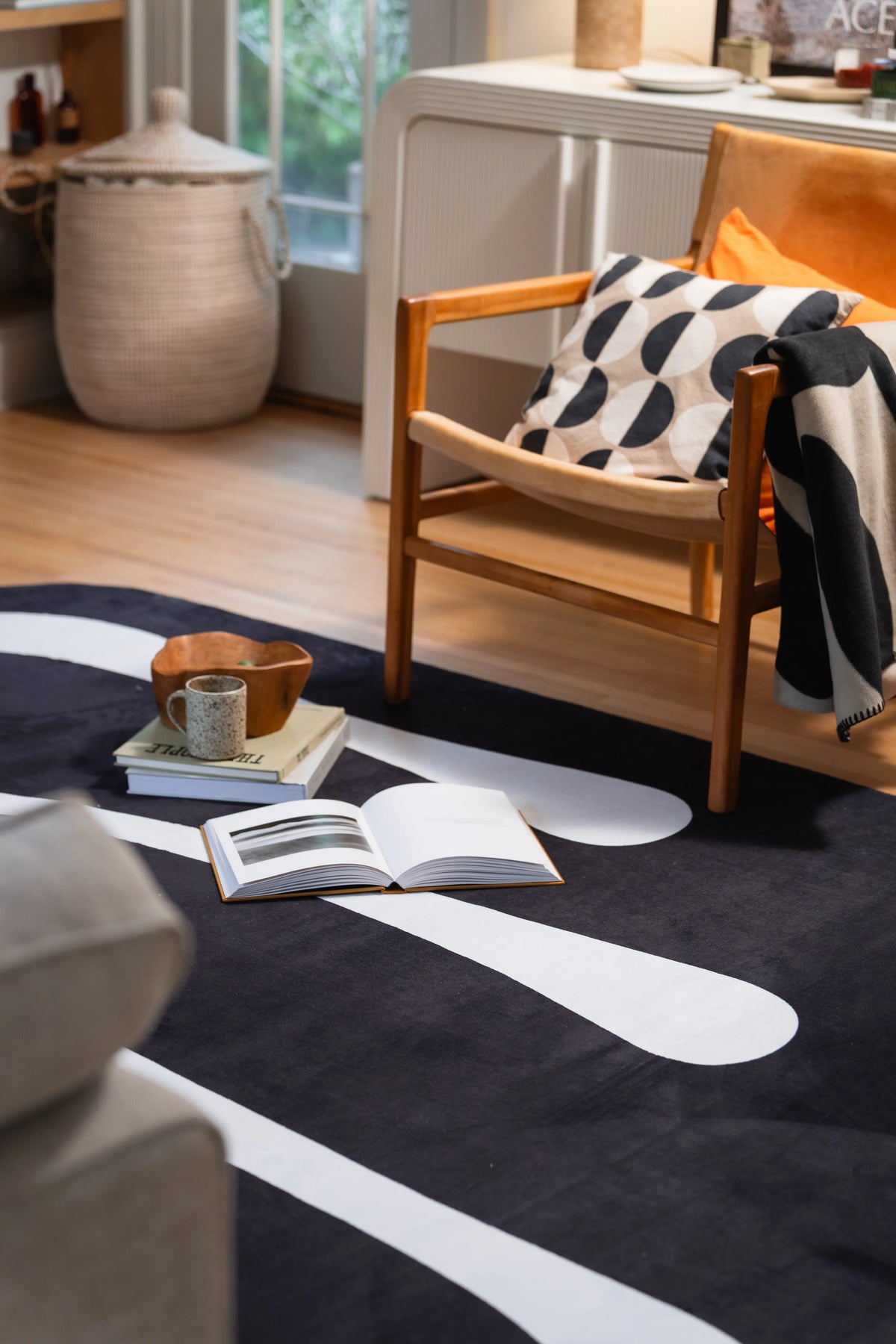 Black and white area rug beneath a wooden armchair with an open book and wooden bowl nearby.
