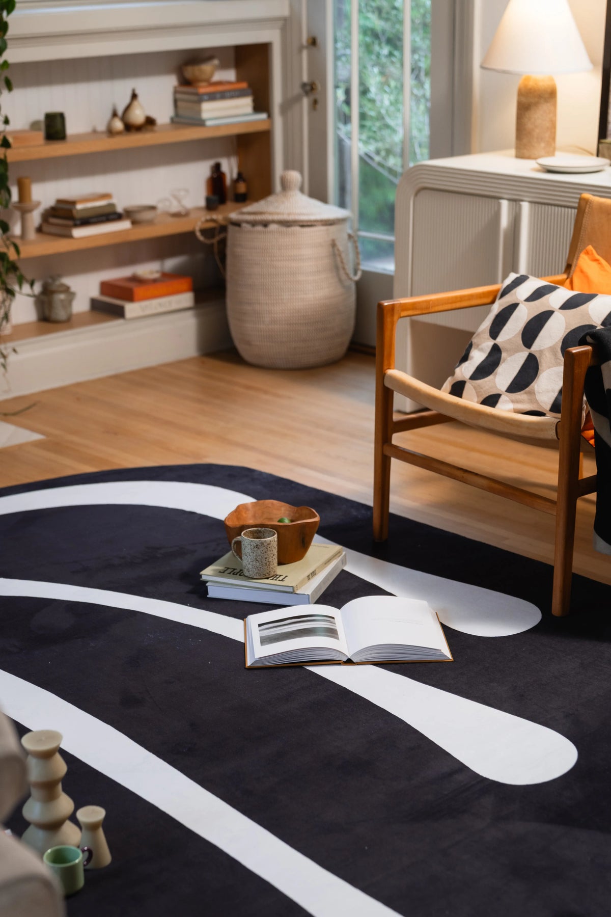 Large black abstract rug beneath a wooden armchair with an open book and small bowl arranged on top.