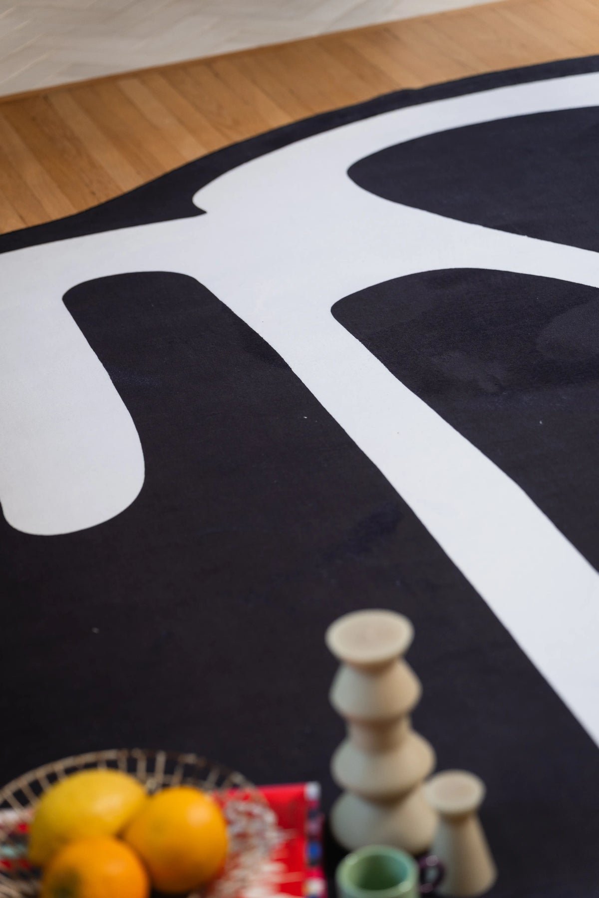 Close-up of white curves on a black rug with oranges and sculptural candles in the foreground.