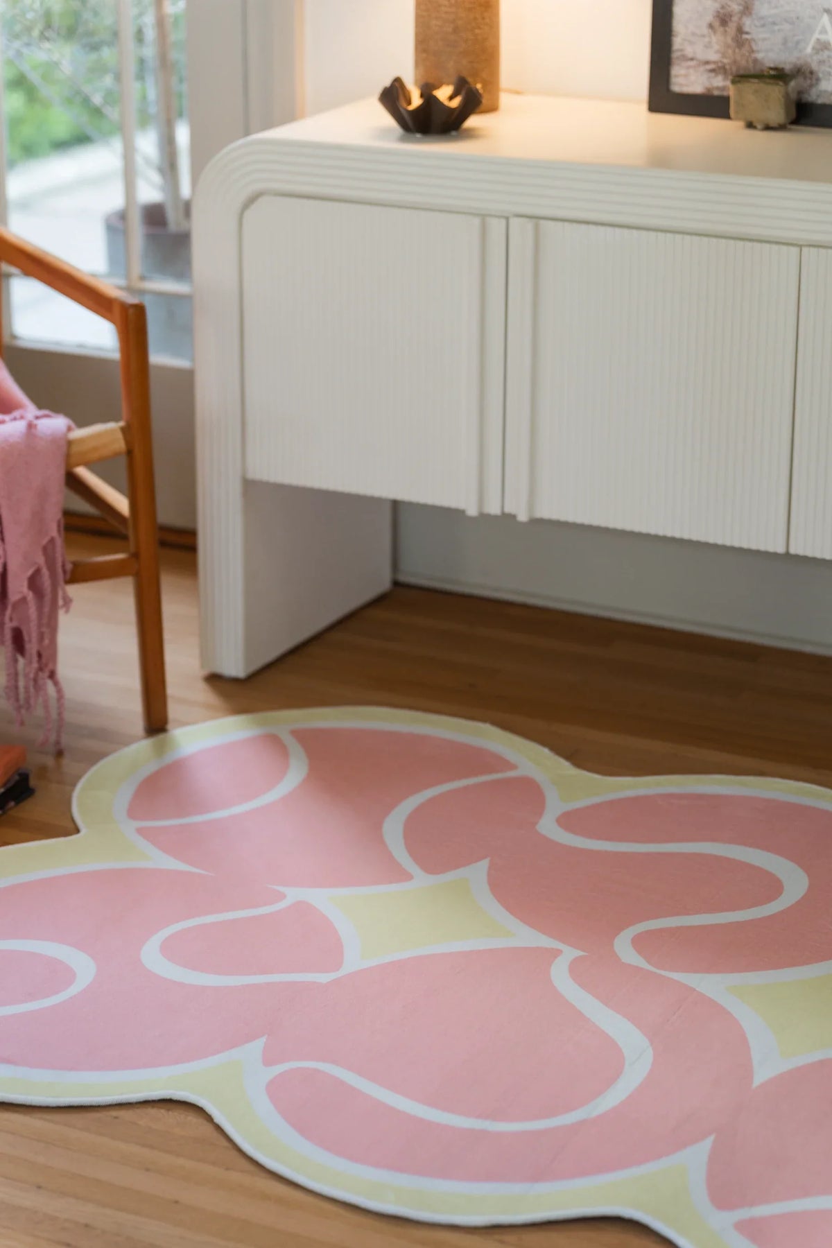Partial view of the pink rug on a light wood floor, with flowing white lines and rounded shapes