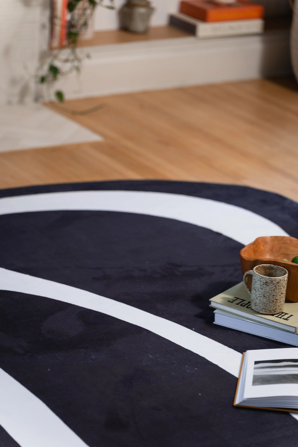 Flowing white stripe across a black area rug beside stacked books and a patterned mug.