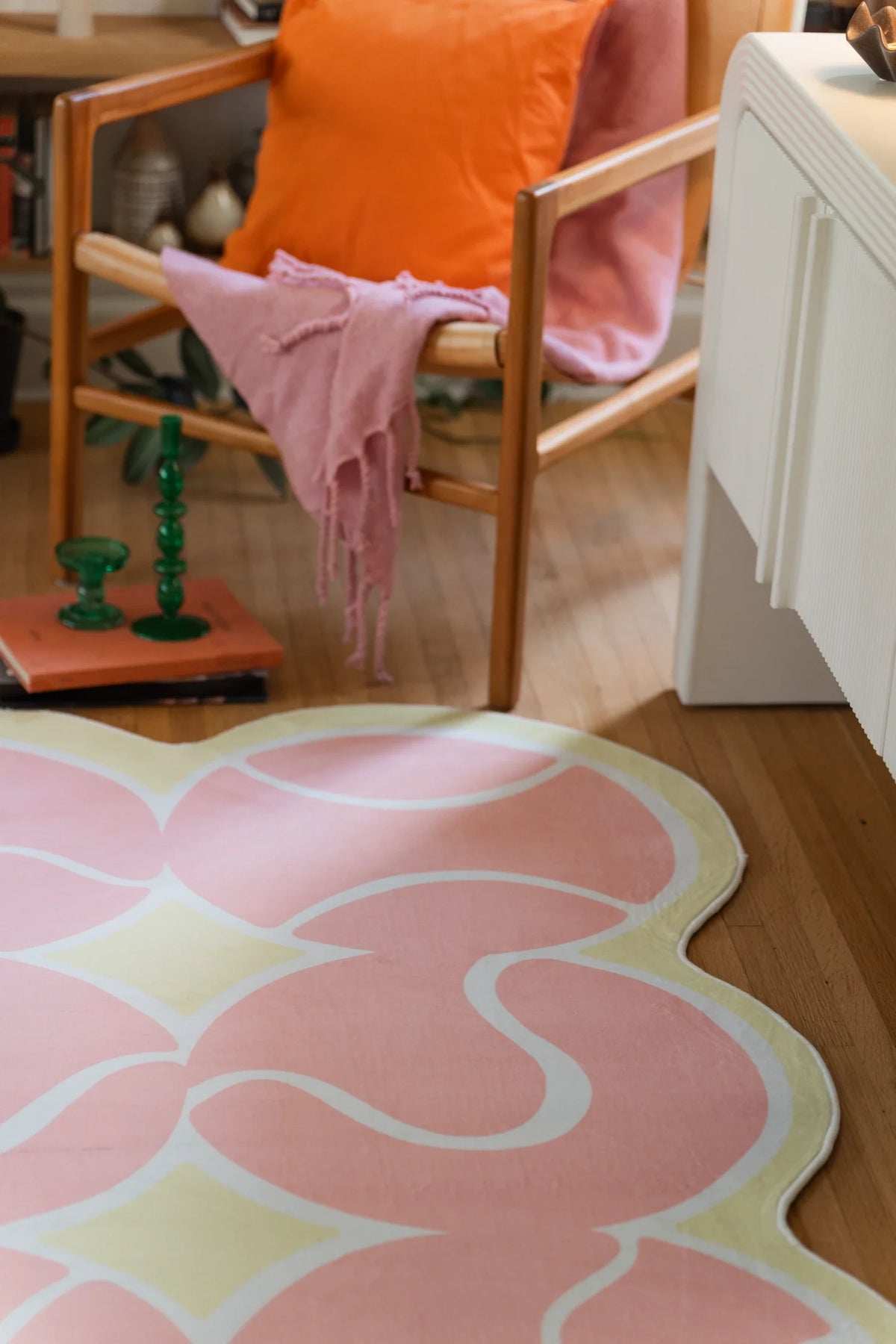 Pink irregular rug beneath a wood chair with an orange cushion and draped pink throw