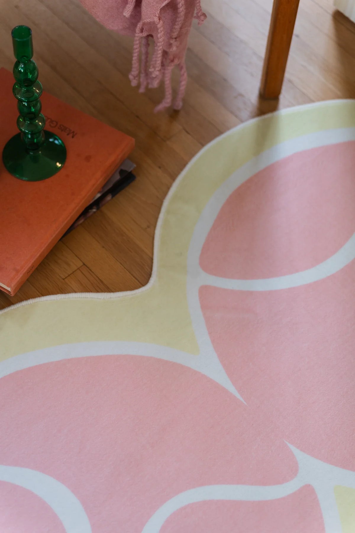 Corner detail of the pink tennis rug beside a green lamp and orange side table on a light wood floor
