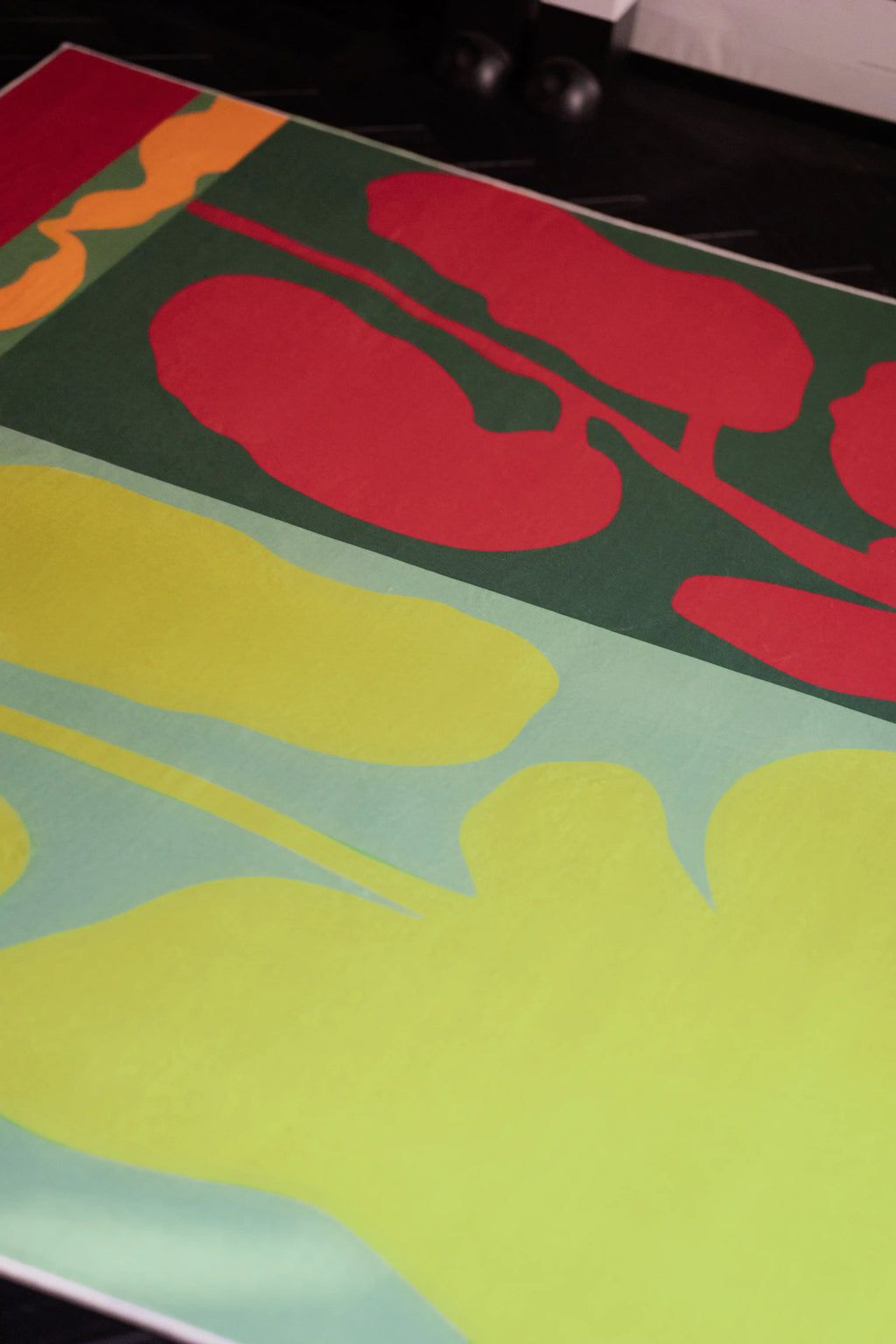 Close up of the graphic floral rug with red flower silhouettes and pale green leaf forms on a dark green ground