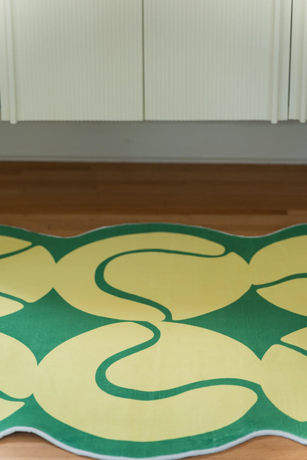 Partial view of the yellow tennis rug on a light wood floor in front of a white cabinet