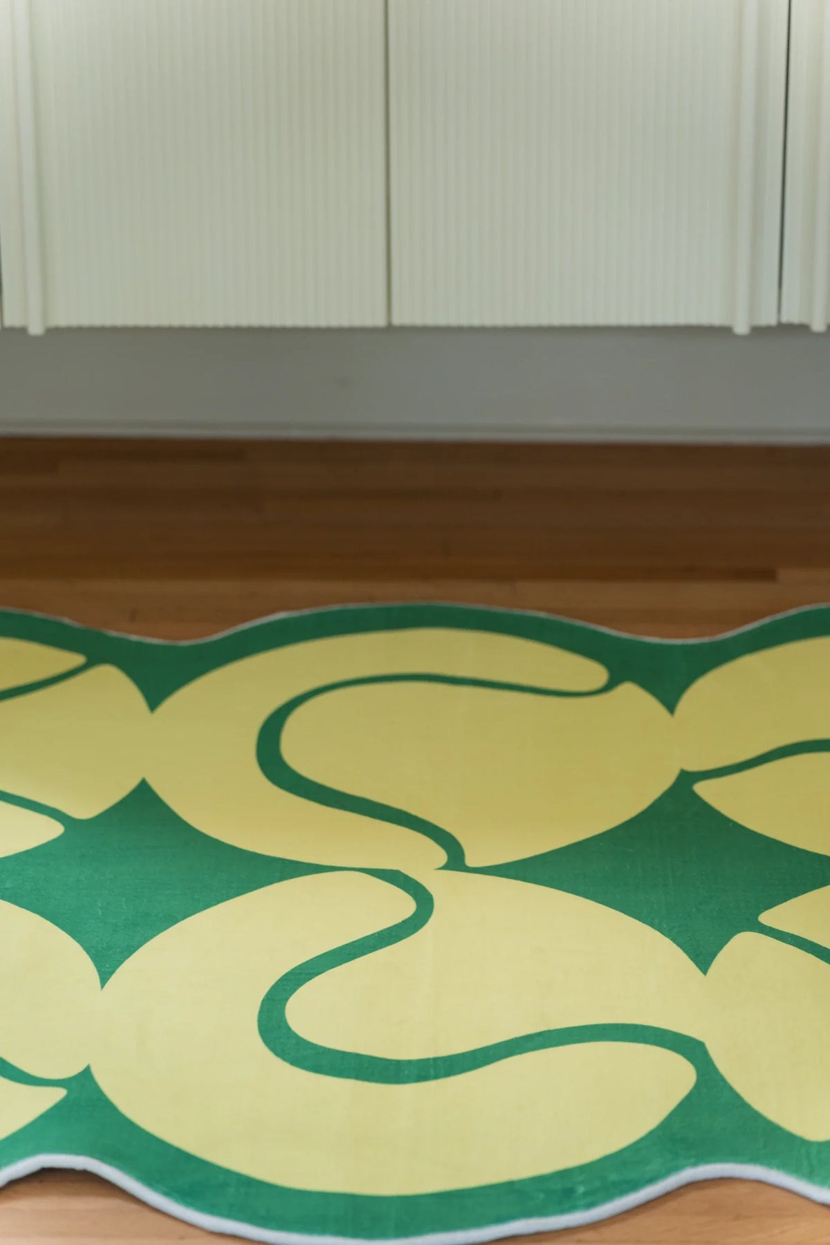 Partial view of the yellow tennis rug on a light wood floor in front of a white cabinet