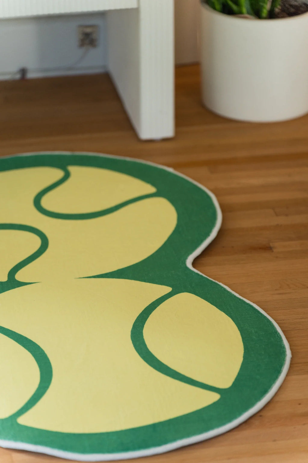 Yellow tennis rug near a white cabinet and planter, with rounded ball like shapes outlined in green