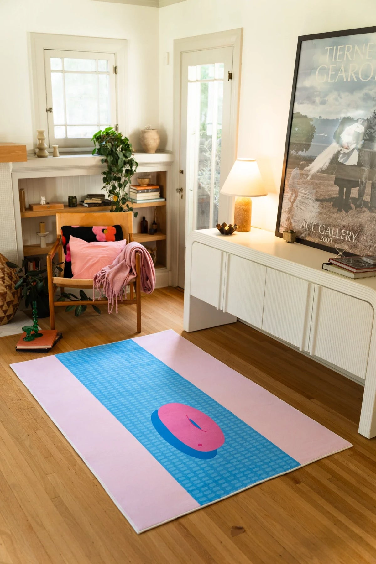 Blue and pink graphic runner rug stretched across a light wood floor in a cozy room with a white cabinet and wood chair