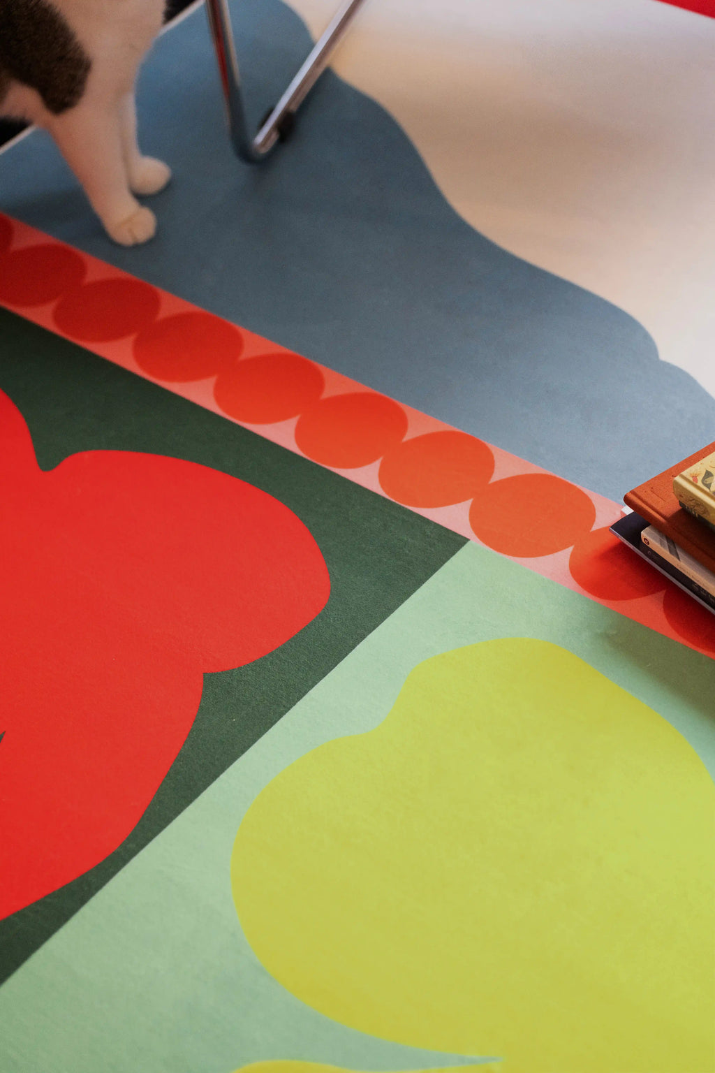 Partial view of the rug with a red flower, pale blue field, orange dot border, and cat paws at the edge