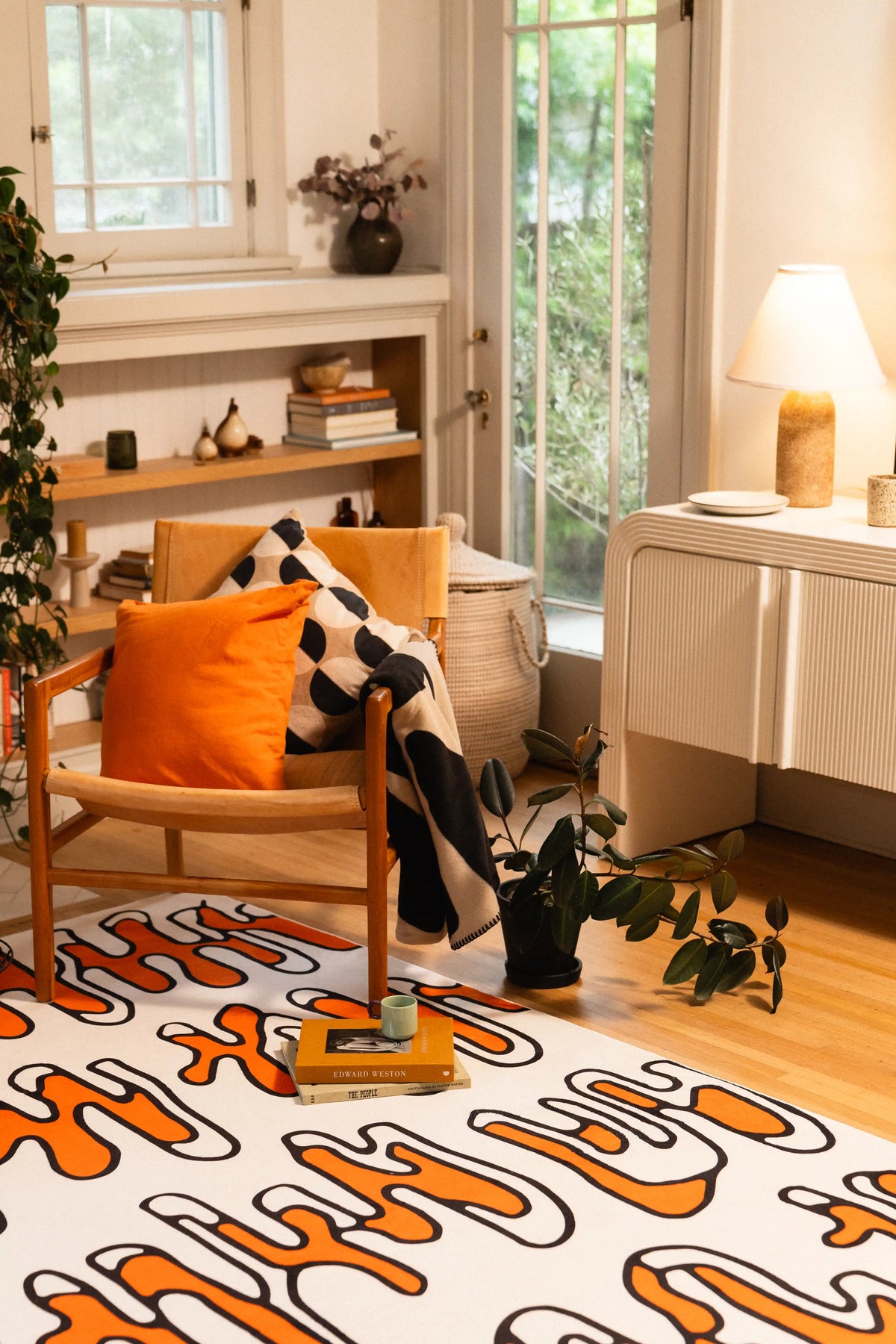 Beige rug with orange and black looping lines beneath a wooden chair with an orange cushion.